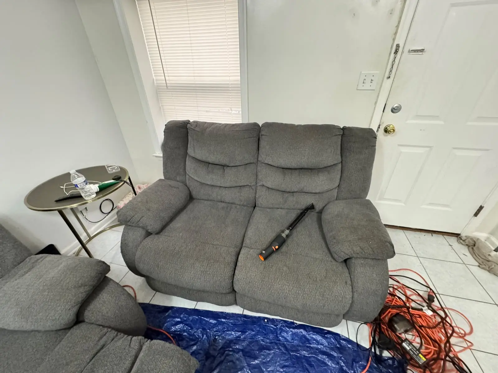 Gray loveseat prepared for professional upholstery cleaning with extraction tool on site